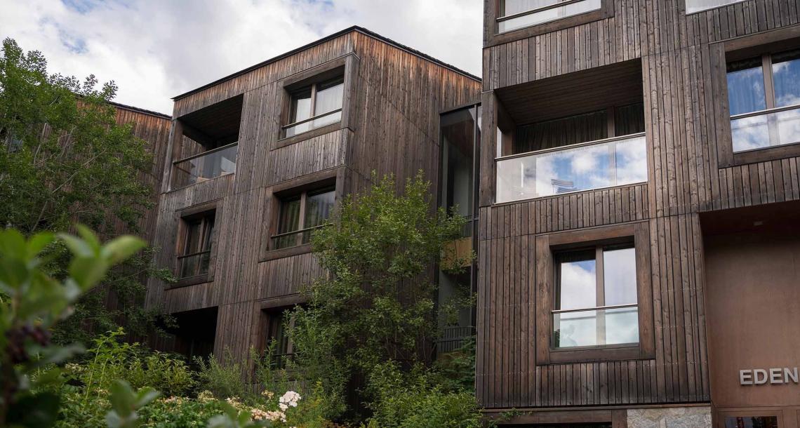 Edificio moderno in legno con ampie finestre e vegetazione circostante.