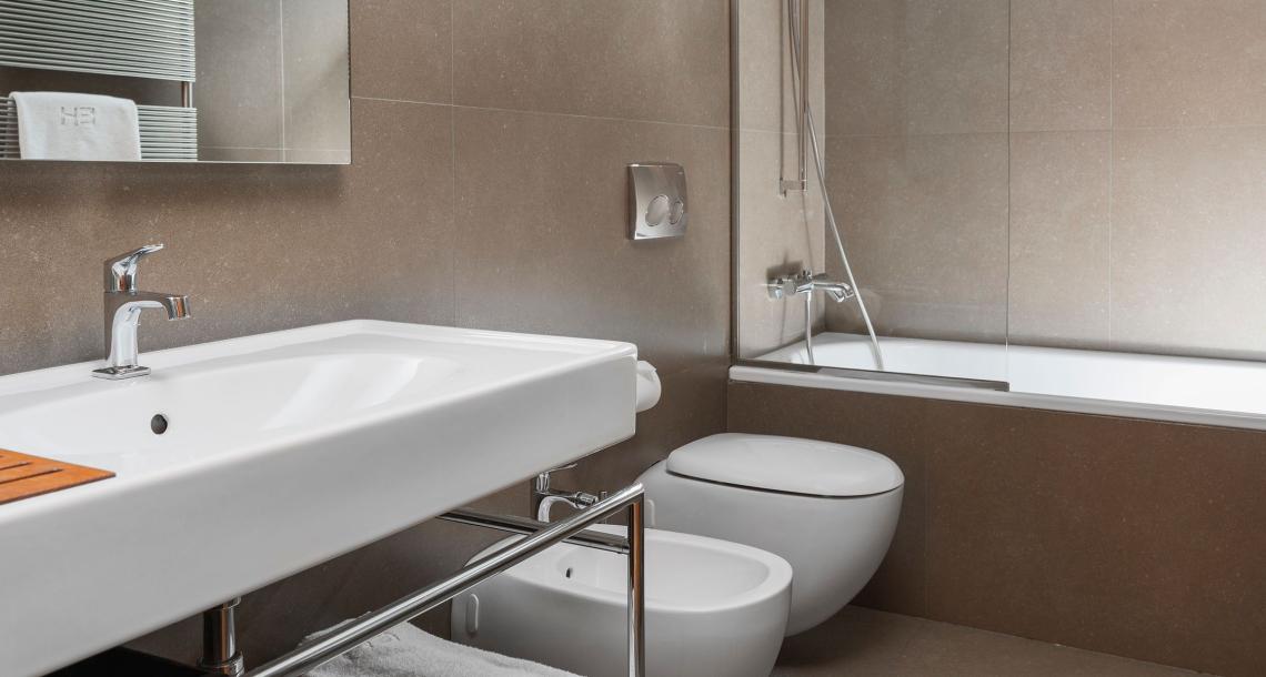 Bagno moderno con lavabo, bidet, doccia e rivestimenti in tonalità neutre.