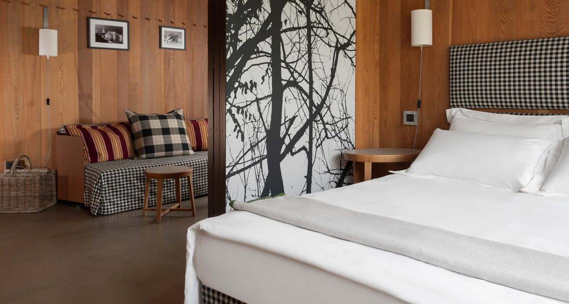 Camera con letto, divano a quadri e parete decorata con albero stilizzato.