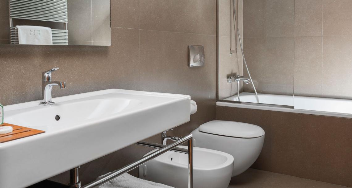 Bagno moderno con vasca, lavabo, bidet e wc, decorato con piastrelle marroni.