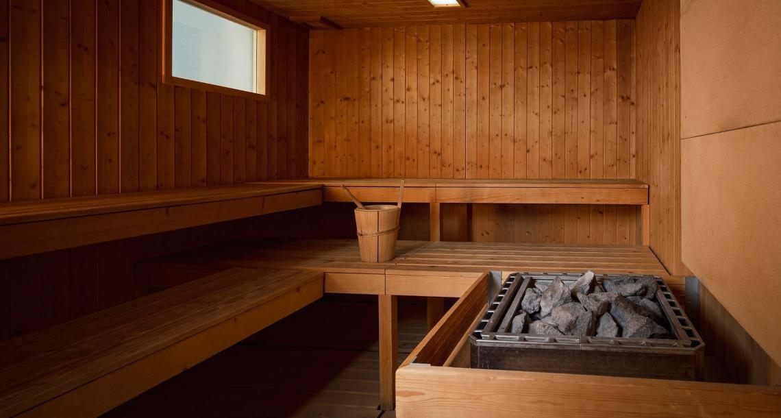 Sauna in legno con panche, secchio e pietre riscaldanti.