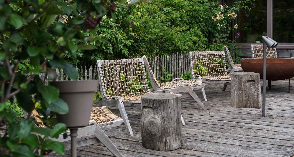 Terrazza con sedie in legno e corda, tronchi come tavolini, e vegetazione circostante.