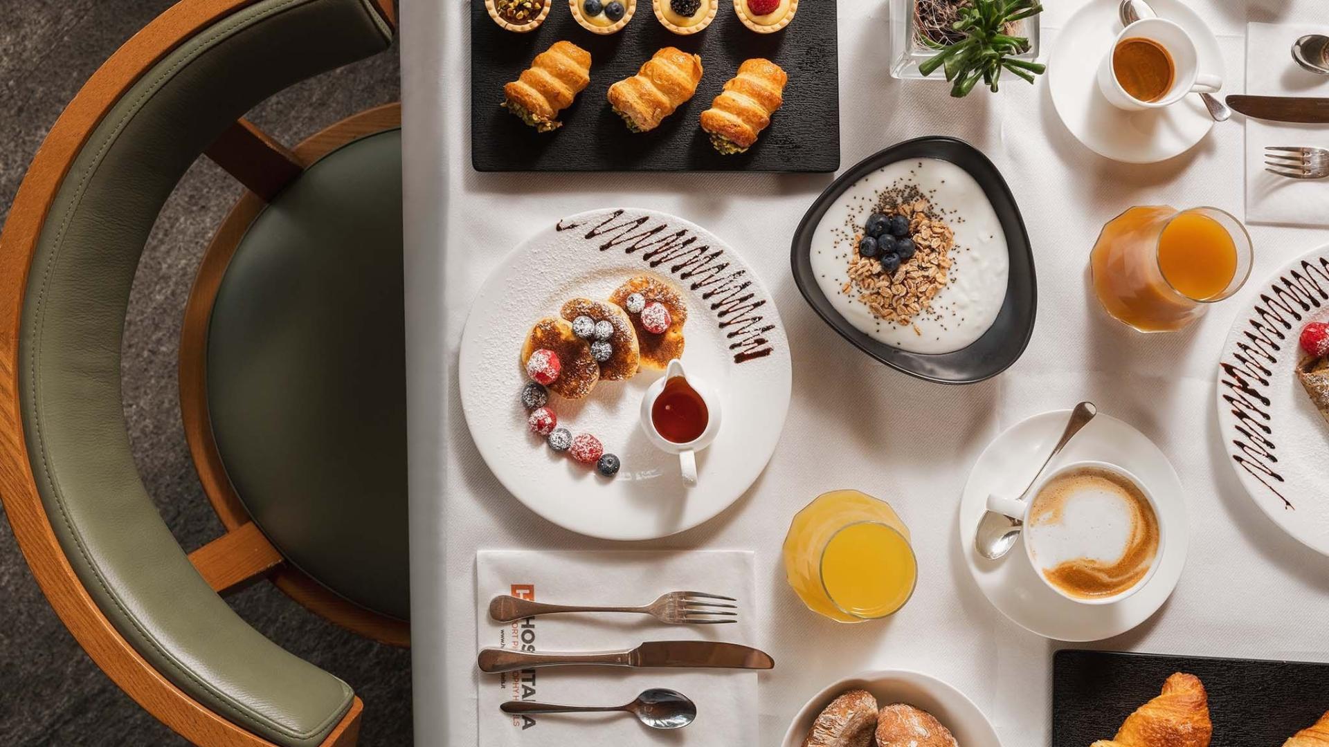 Colazione elegante con dolci, yogurt, succo d'arancia e caffè su tavola apparecchiata.