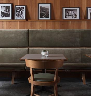 Interno di caffetteria con sedie in legno, tavolo e foto in bianco e nero.