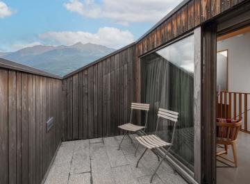 Terrazza con sedie pieghevoli, vista montagna, pareti in legno e porta scorrevole in vetro.