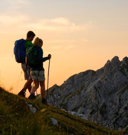 Due escursionisti al tramonto su una montagna con zaini e bastoni da trekking.